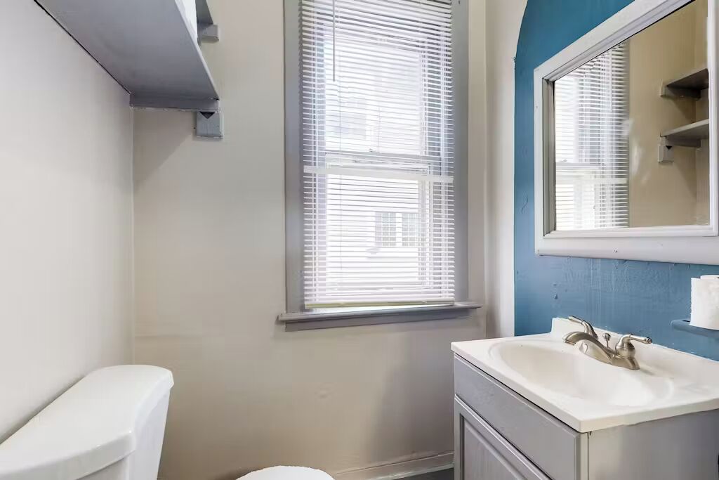 A bathroom with a toilet, sink, and window with blinds.