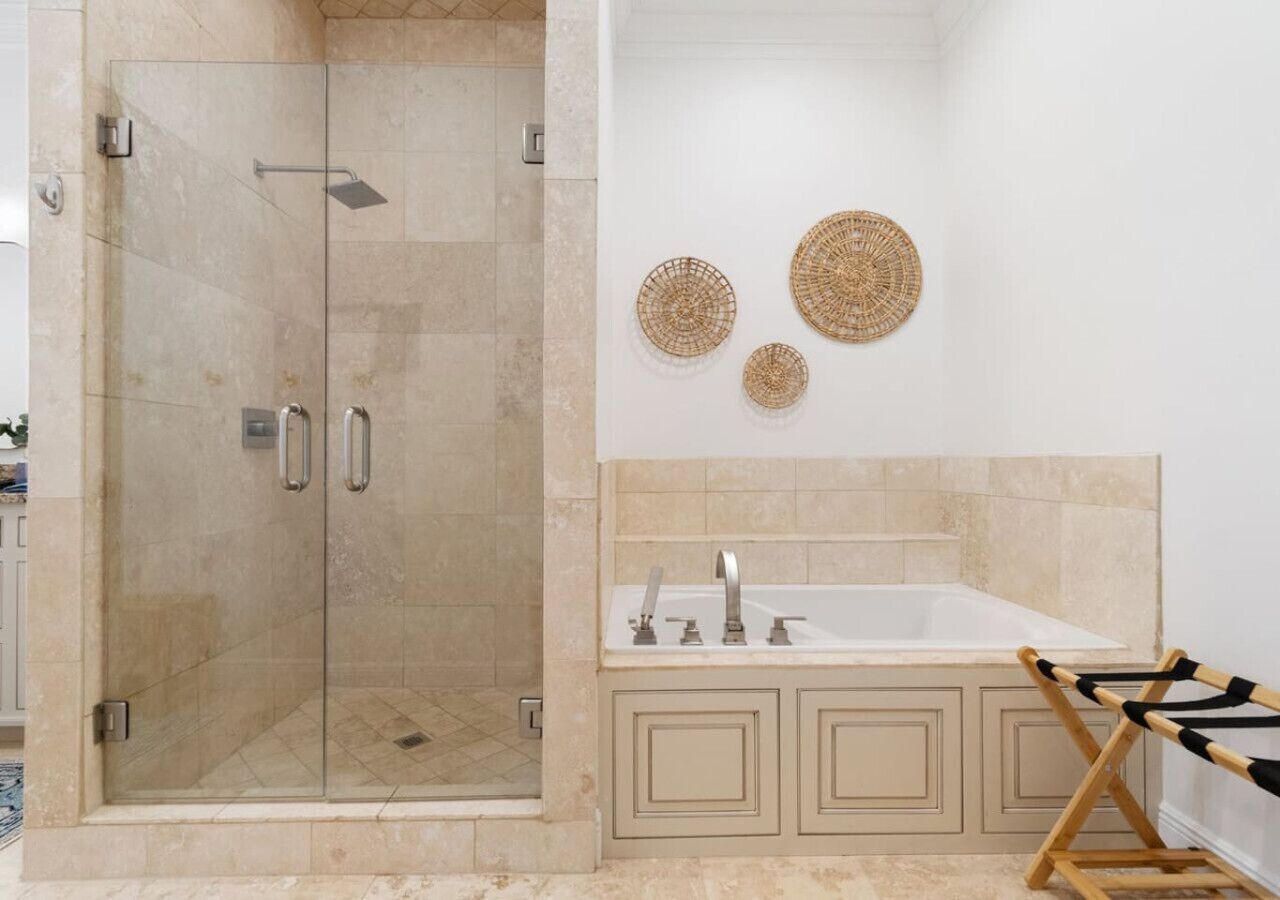 Une salle de bain avec une douche à parois de verre, un lavabo blanc et des meubles de couleur beige. Trois éléments décoratifs en fibres tressées ornent les murs.