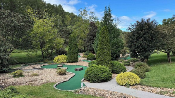 Un campo de golf con un putting green serpenteante, rodeado de setos y árboles bien cuidados.
