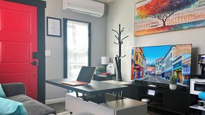 Un salon moderne avec une porte rouge, un ordinateur portable sur un bureau, un téléviseur et une machine à café.
