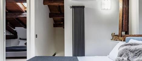A bedroom with a bed, a radiator, and a wooden ceiling.