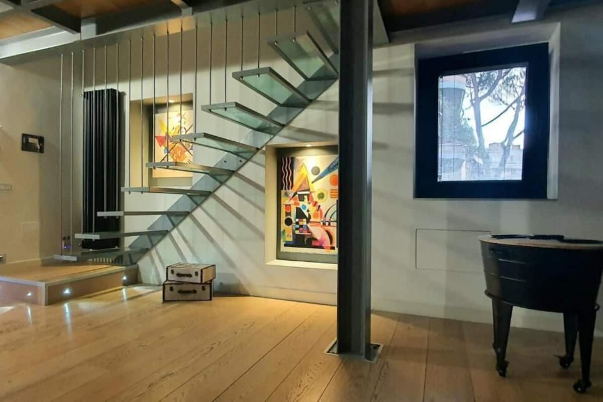 A modern interior with a wooden floor, a staircase with glass railings, a piano, and abstract art on the walls.