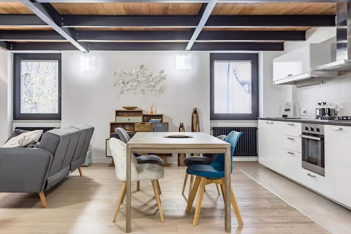 A modern kitchen with white cabinets, stainless steel appliances, and a wooden dining table with chairs.