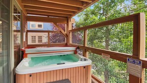 A hot tub on a wooden deck with a safety sign, surrounded by a mesh fence and trees. - Cozy Old Town Escape with Hot Tub and Mountain Views 201B (Park City)