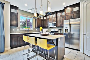 A modern kitchen with dark wood cabinets, stainless steel appliances, and a central island with yellow bar stools. - Entrada at Moab 424 (Moab)