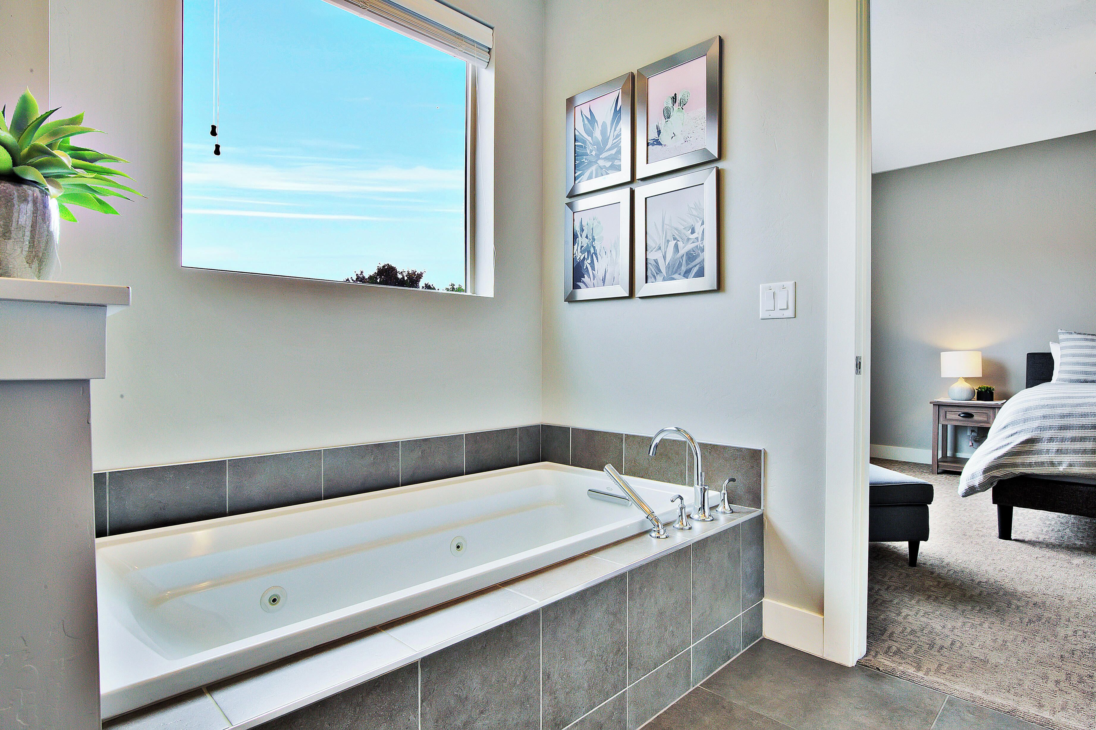 A modern bathroom with a large bathtub, a window, and a wall-mounted mirror.