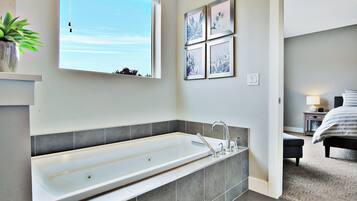 A modern bathroom with a large bathtub, a window, and a wall-mounted mirror.