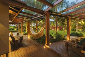 A wooden deck with a hammock, wooden chairs, and a glass ceiling. - Santi Sabai Ibira - Um Refúgio às Margens da Lagoa (Imbituba)