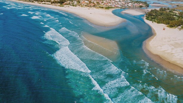 Vista aérea de una zona costera con aguas azul turquesa, playas de arena y un pueblo distante.