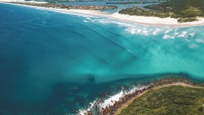 An aerial view of a coastal area with clear blue waters, sandy beaches, and green hills. - Santi Sabai Ibira - Um Refúgio às Margens da Lagoa (Imbituba)