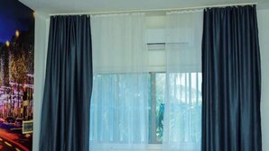 A room with a large window, dark curtains, a wooden table, and two chairs.