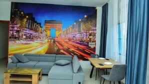 A living room with a large mural of the Arc de Triomphe, a gray sofa, a wooden coffee table, and a dining area with a table and chairs.