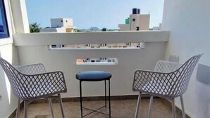 A balcony with two chairs and a small table, offering a view of buildings and a clear sky.