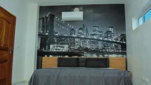 Une chambre à coucher avec un lit, une fresque représentant un paysage urbain sur le mur et une fenêtre.