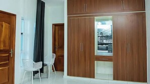 Une pièce avec une grande armoire en bois, une chaise blanche et un rideau noir.