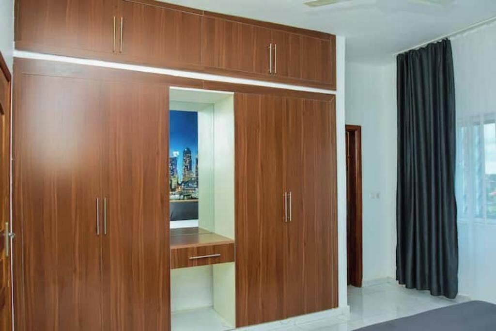 Una habitación con un armario de madera, un banco y vistas a un paisaje urbano a través de una puerta abierta.