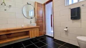 Une salle de bain avec un meuble-lavabo en bois, un miroir rond, un lavabo blanc et un sol carrelé de carreaux noirs.