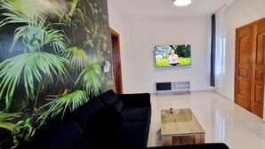 A modern living room with a black sofa, a wooden coffee table, and a large TV screen. - Jungle Sensation (Lomé)