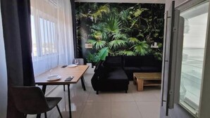 A room with a dining table, a black sofa, a small coffee table, and a large potted plant. - Jungle Sensation (Lomé)