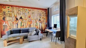 Un salon comprenant un canapé, une table basse et un bureau avec une chaise. Un mur est décoré d’une fresque représentant des hiéroglyphes égyptiens.