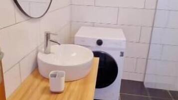 A bathroom with a wooden vanity, a white sink, a mirror, and a washing machine.