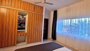 A bedroom with a wardrobe, a bed, and a large window.