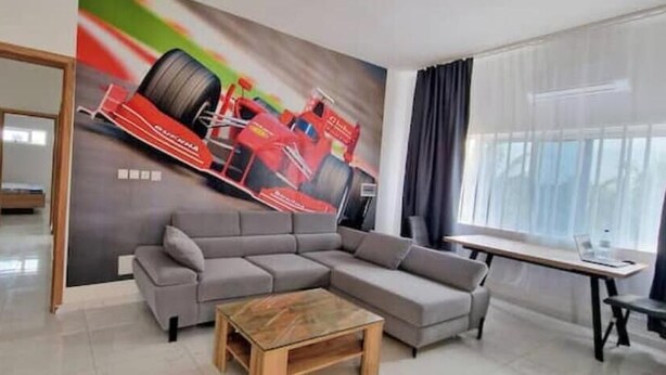 A modern living room with a grey sectional sofa, a wooden coffee table, and a large racing car mural on the wall.