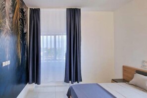 A hotel room with a bed, a nightstand, and a window with curtains. - Voltiges.. (Lomé)