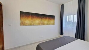 Una habitación de hotel con una cama, un cuadro abstracto grande en la pared y una ventana con cortinas.
