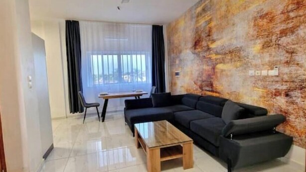 Una sala de estar moderna con un sofá modular, una mesa de centro de madera y un ventanal con cortinas translúcidas.