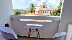 Un balcón con dos sillas blancas y una mesita, con vistas a edificios y palmeras.
