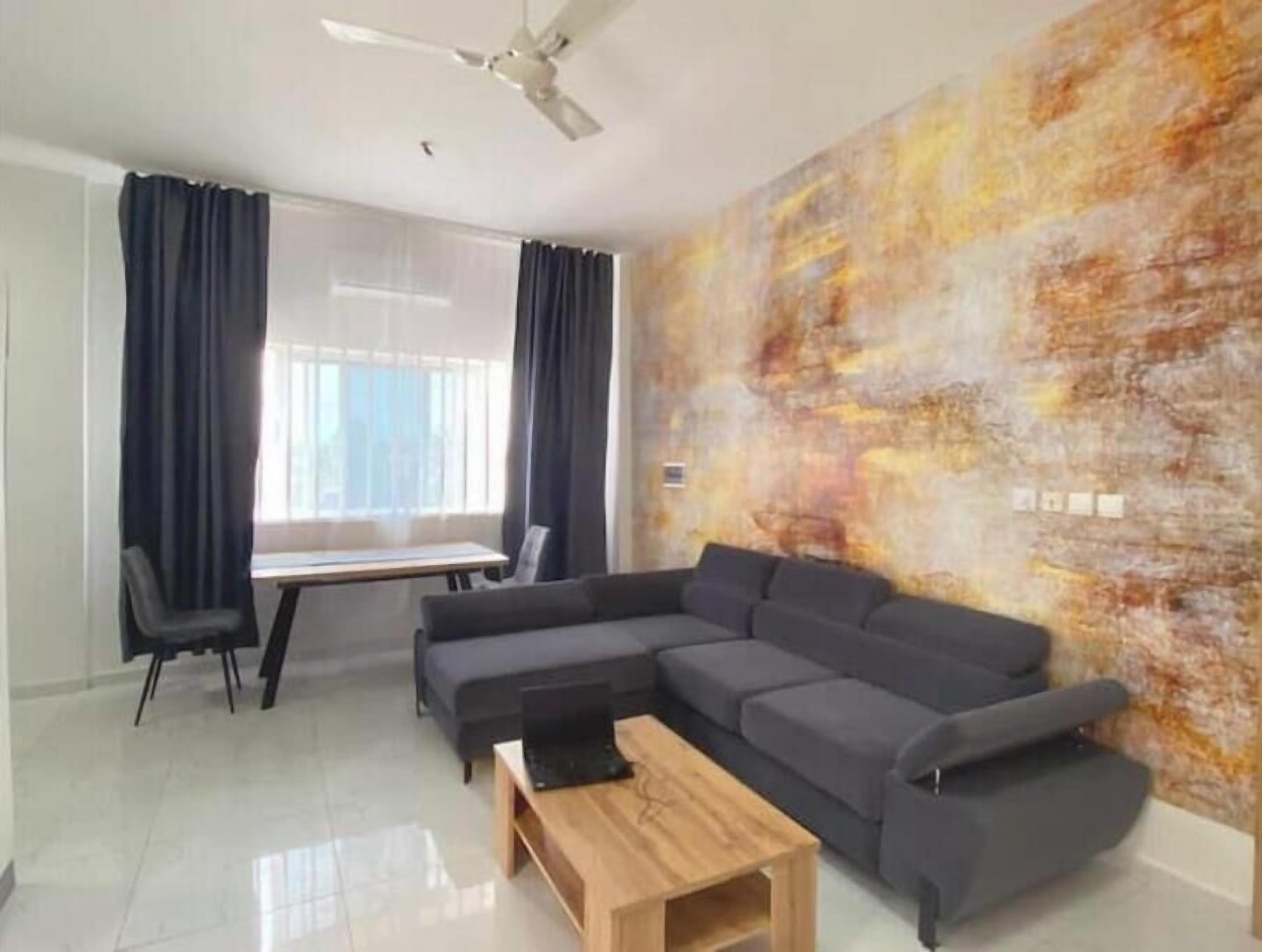 A modern living room with a sectional sofa, a wooden coffee table, and a large abstract mural on the wall.