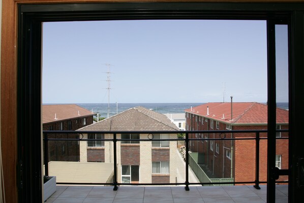 A view from a balcony with a clear sky, buildings with red roofs, and a distant view of the sea.