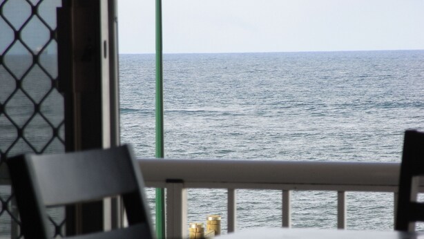 A view of the sea from a balcony with a table and chairs in the foreground. - Welcoming 2-bedroom apartment in The Entrance (The Entrance)
