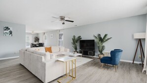 A modern living room with a white sofa, a blue armchair, a TV, and a ceiling fan. - Cozy Home Plainfield Indy (Plainfield)