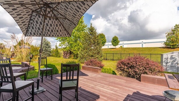 A wooden deck with outdoor furniture, including chairs and a table, under a patterned umbrella. - Cozy Home Plainfield Indy (Plainfield)