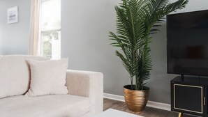 A living room with a beige sofa, a large potted plant, a television, and a minimalist cabinet. - Cozy Home Plainfield Indy (Plainfield)