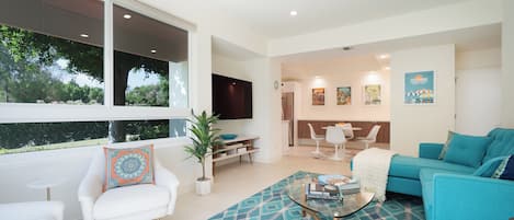 Una sala moderna con sofá, sillón y mesa de centro. Hay un comedor con mesa y sillas, y una cocina al fondo.