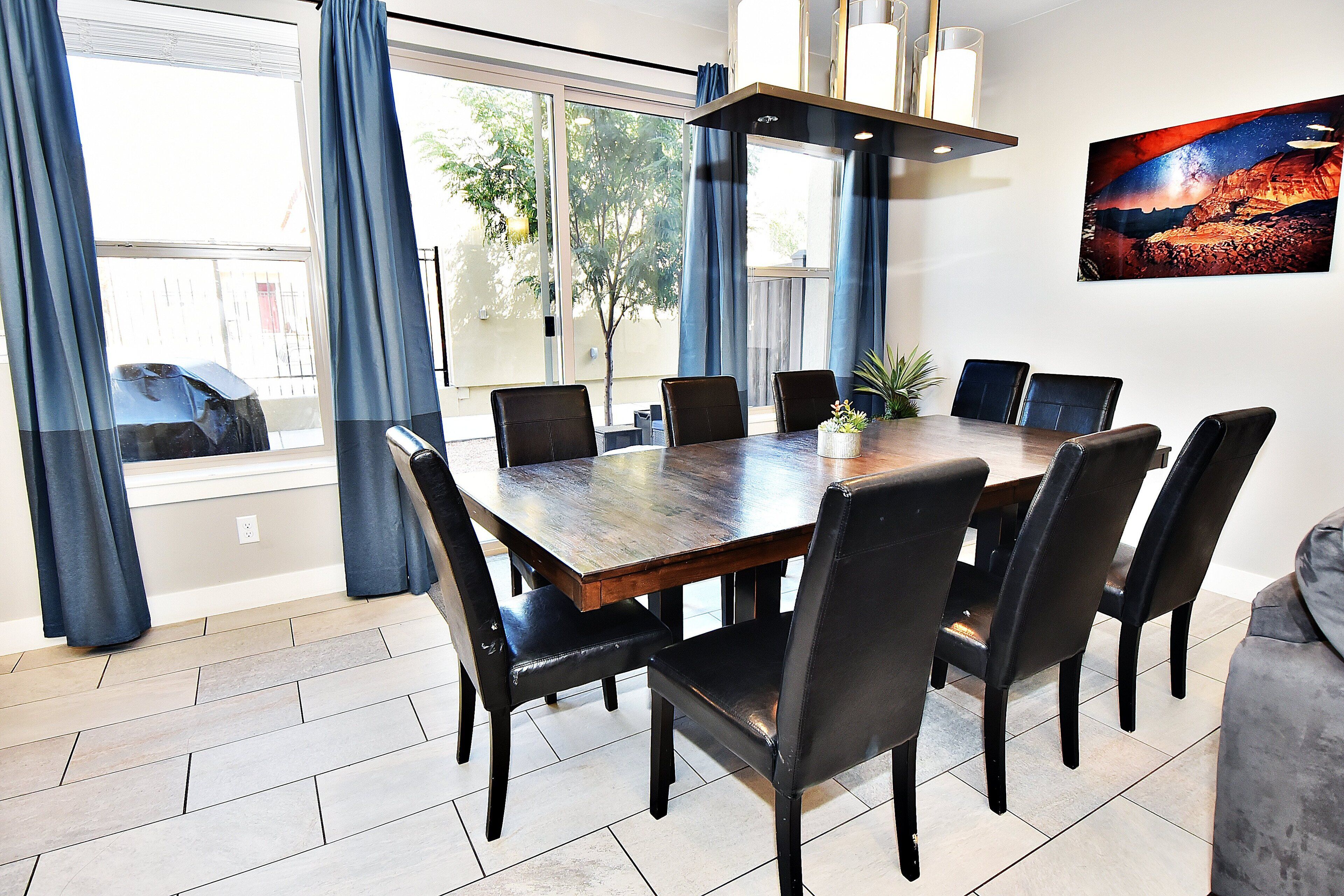 A dining area with a large wooden table and black chairs, a potted plant, and a painting on the wall.