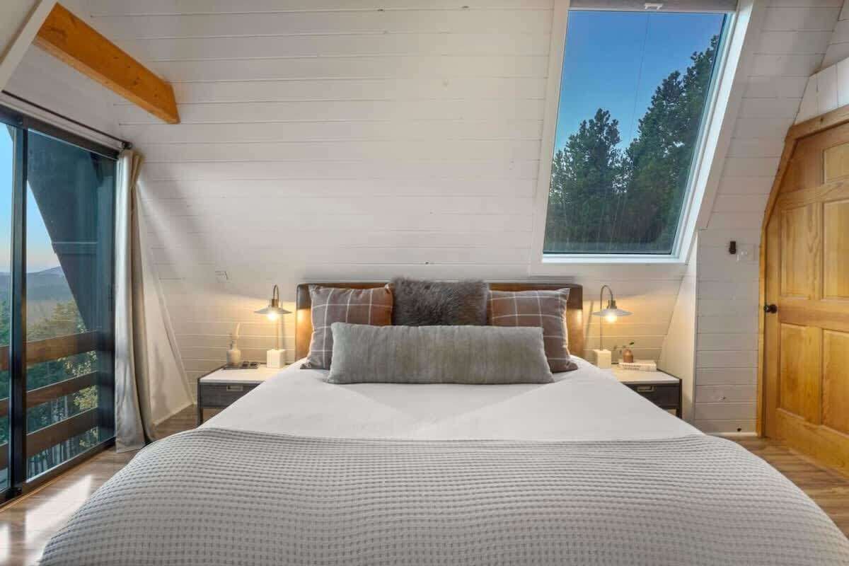A bedroom with a large bed, two bedside tables, a skylight, and a view of trees.