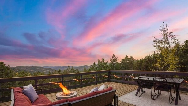 Una terraza de madera con sofá, mesa y sillas, con vistas a un paisaje pintoresco.