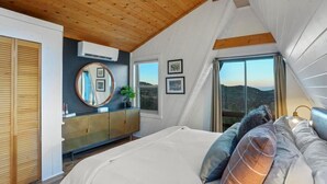 Un dormitorio con una cama grande, techo de madera, cómoda y vistas al exterior.