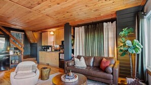 Una sala de estar acogedora con techo de madera, un sofá de cuero marrón, un sillón blanco y una mesa de centro.