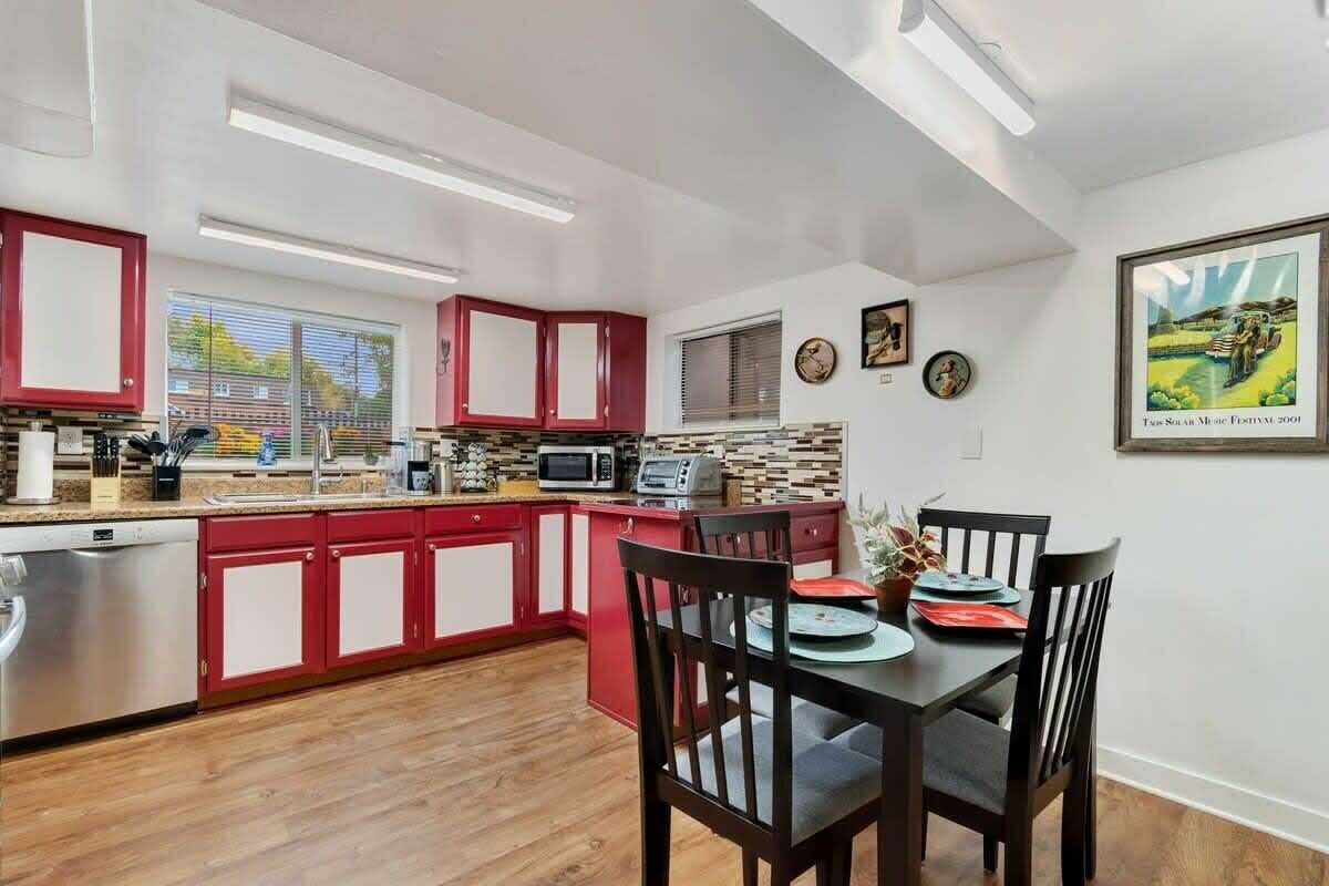 Una cocina moderna con gabinetes rojos, un comedor con mesa y sillas, y un cuadro enmarcado en la pared.