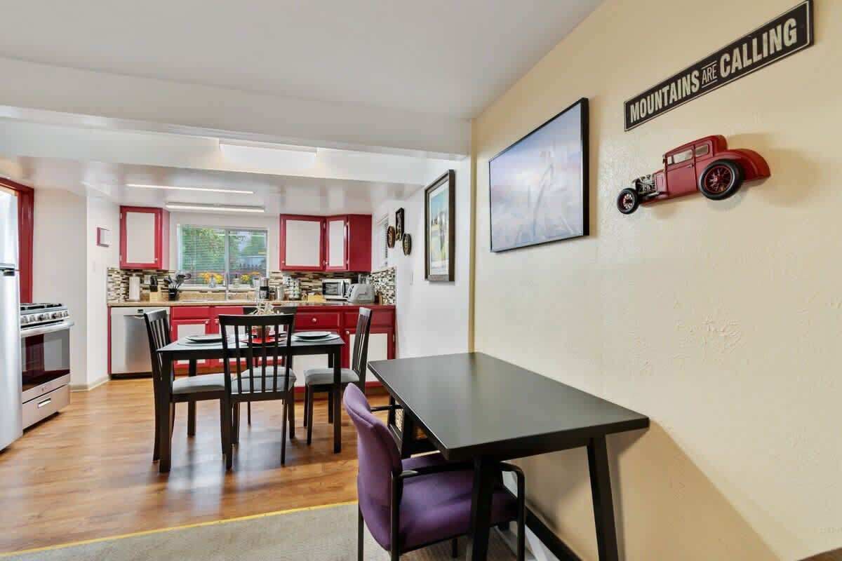 Una cocina moderna con armarios rojos, una zona de comedor con mesa y sillas, y un letrero en la pared que dice 'MOUNTAINS ARE CALLING'.