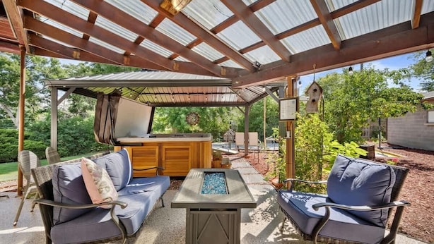 An outdoor patio area with a covered seating area, a fire pit, and a wooden table. - Pickleball Retreat | Hot Tub & Games (Denver)