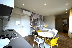 A modern hotel room with a kitchenette, a bed with a grey headboard, a round dining table with yellow chairs, and a large leaf-patterned wall. - Skyline Sunshine (Apartment with Terrace)   (Siena)