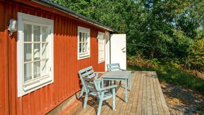 Eine Holzhütte mit einer Terrasse, zwei Fenstern und einem Kühlschrank.