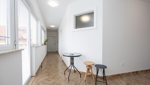 A hallway with a tiled floor, a round table with a stool, and a window with blinds.