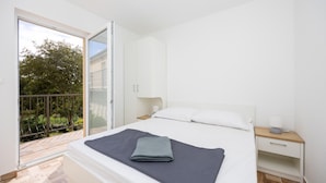 A bedroom with a bed, a nightstand, a window, and a door leading to a balcony.